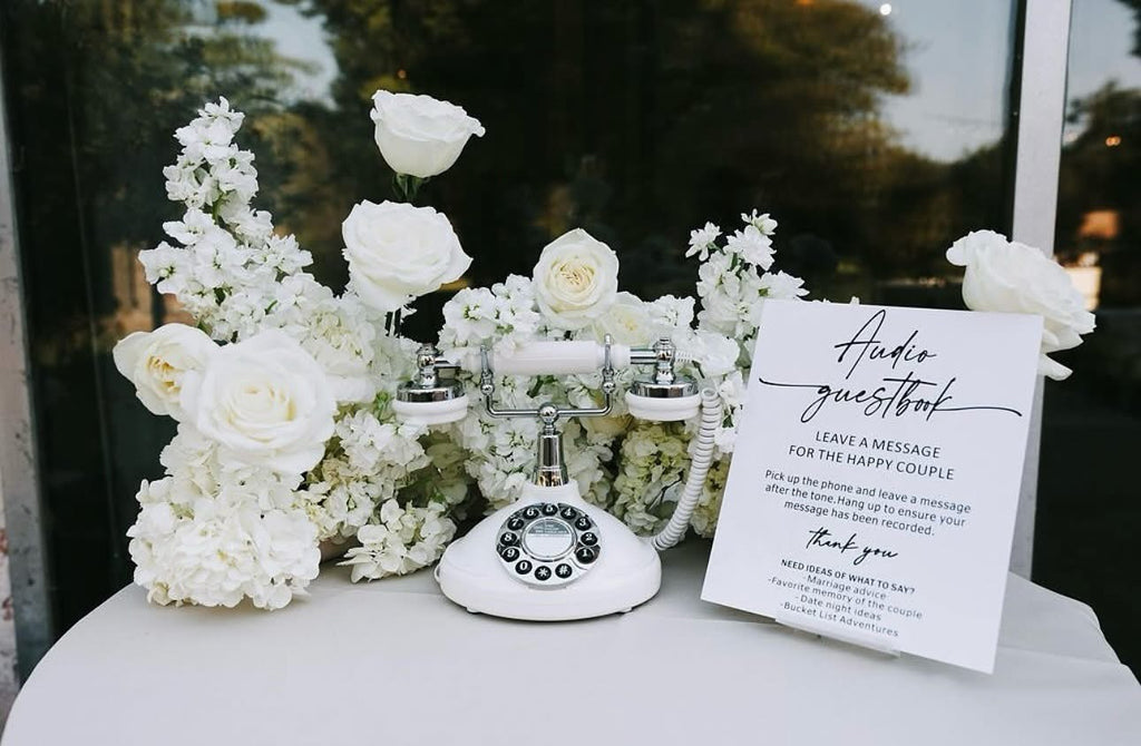 Vintage-style phone with white flowers and a guestbook on a table outdoors.