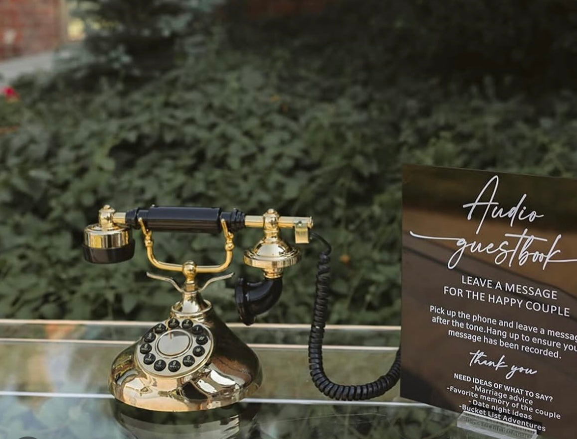 Vintage-style telephone on a glass surface with a card labeled 'Audio guestbook' in front of greenery.