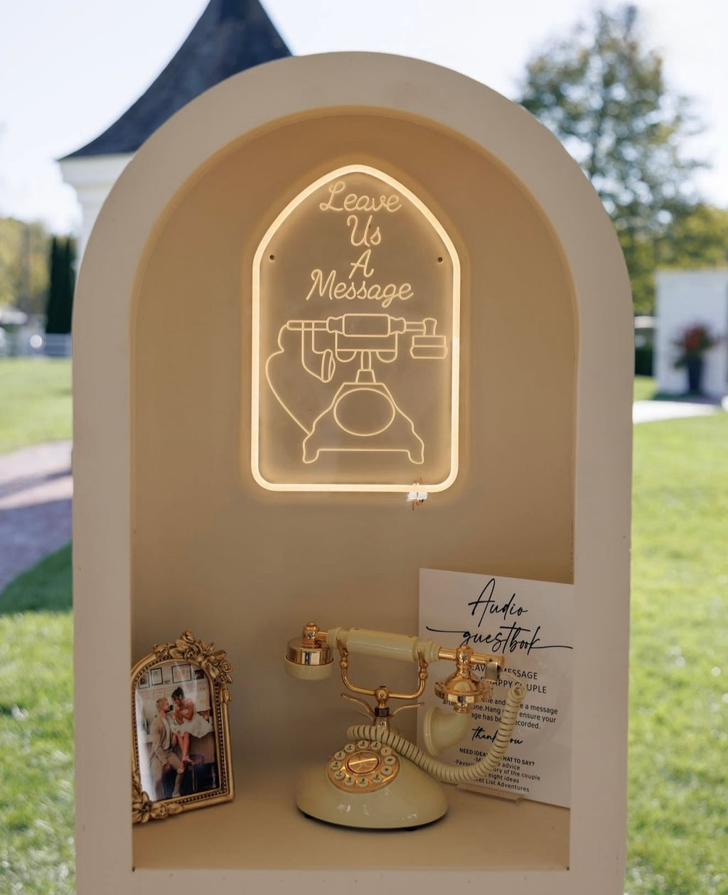 Decorative display with a vintage phone, neon sign, and photo frame outdoors.