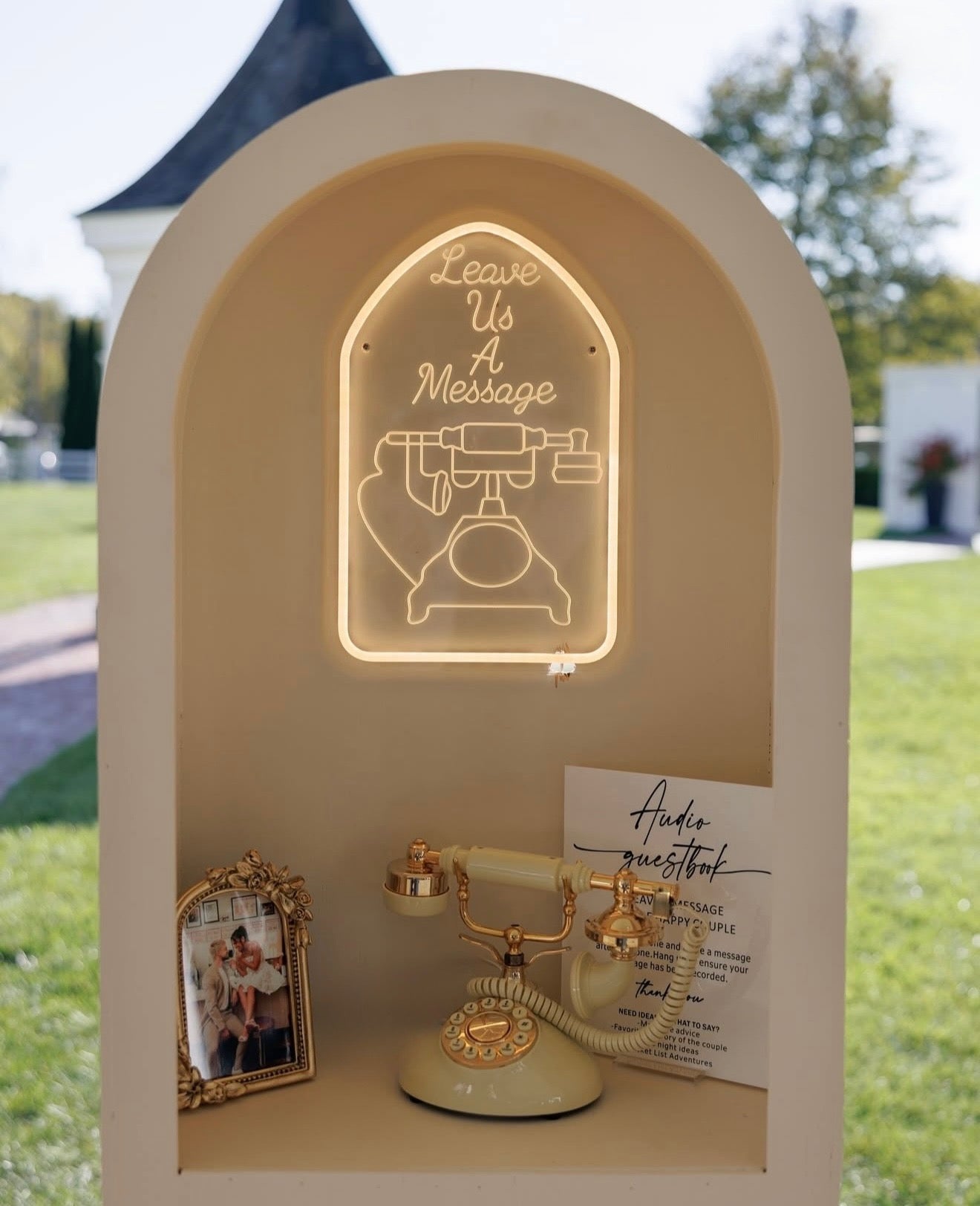 Decorative display with a vintage phone, neon sign, and photo frame outdoors.